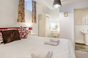 Ein Hotelzimmer mit Bett, Nachttisch, Lampe, Kleiderschrank, Spiegel und Badezimmer mit Waschbecken.