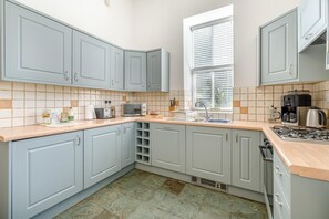 Eine Küche mit hellblauen Schränken, einer Arbeitsplatte mit verschiedenen Geräten und einem Fenster mit Jalousien.