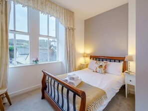 A bedroom with a wooden bed, white bedding, a window with curtains, a bedside table with a lamp, and a view of the outside. - 3 Bed in Hawkshead (oc-llh21) (Hawkshead)