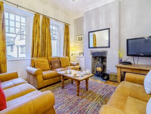 A living room with a sofa set, a fireplace, a television, and a window with curtains. - 3 Bed in Hawkshead (oc-llh21) (Hawkshead)