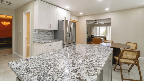 A kitchen with white cabinets, a granite countertop, a refrigerator, and a dining area with chairs. - Chic 5br, Yard, Mtn Views, Games 4 fun Family Time (Albuquerque)