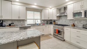A modern kitchen with white cabinets, granite countertops, a stainless steel stove, and a microwave. - Chic 5br, Yard, Mtn Views, Games 4 fun Family Time (Albuquerque)