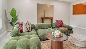 A living room with green upholstered furniture, a wooden coffee table, and a large plant. - Chic 5br, Yard, Mtn Views, Games 4 fun Family Time (Albuquerque)