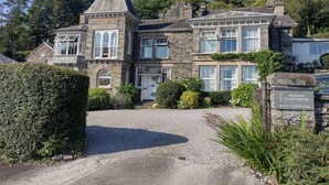 Un edificio de piedra de dos plantas con una torre destacada, un camino de grava y un cartel que indica 'PARKING MAIN HOUSE' y 'COTTAGES'.