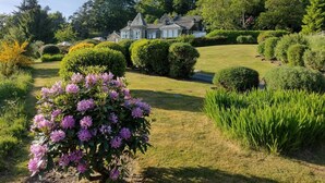 Una casa grande e histórica con un jardín bien cuidado, que incluye setos podados y arbustos florecientes.