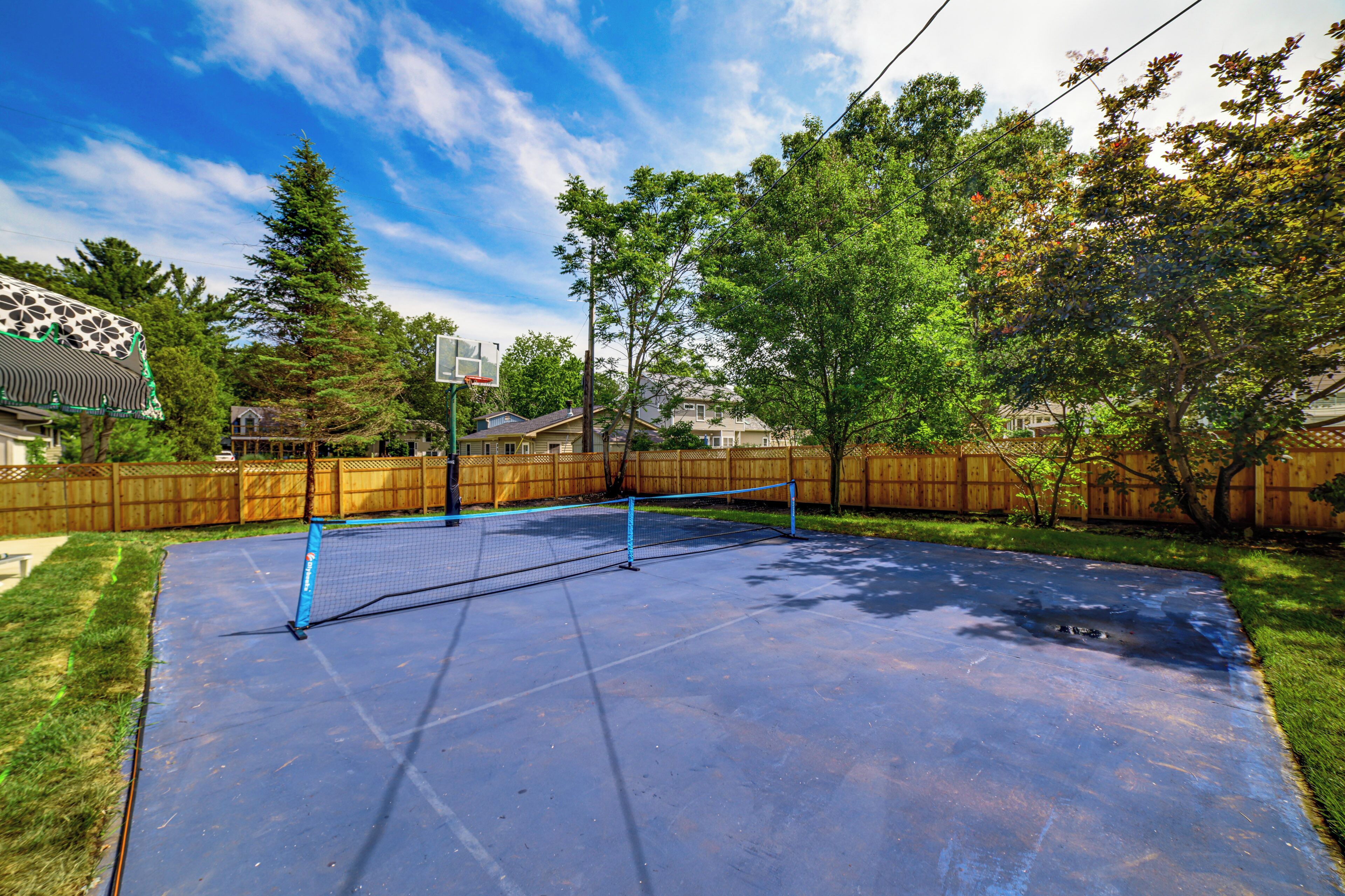 A backyard with a tennis court, wooden fence, and trees.