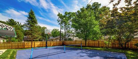 A backyard with a tennis court, wooden fence, and trees.