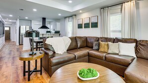 Ein modernes Wohnzimmer mit einem Ledersofa, einem runden Holztisch und einer Küche im Hintergrund.