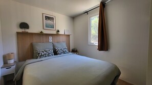 Ein Schlafzimmer mit einem Bett, einem Kopfteil, einem Nachttisch, einem Fenster mit Vorhängen und einem Wandbild.