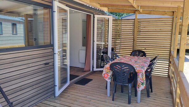 Ein überdachter Außenbereich mit Tisch und Stühlen, einer Schiebetür aus Glas und einer Holzterrasse.
