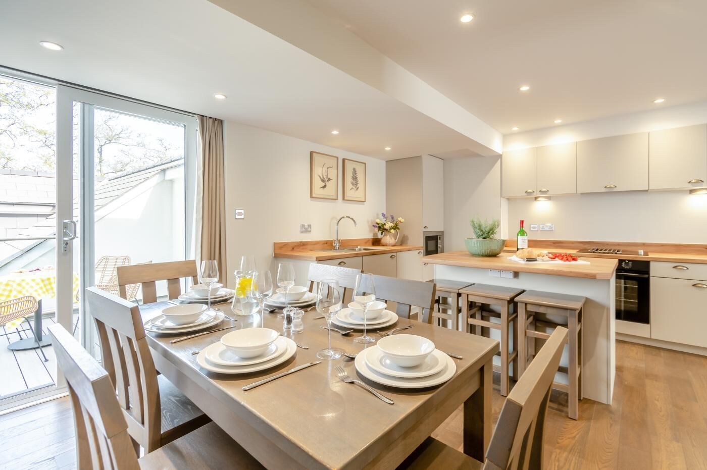 A modern kitchen with wooden countertops, a dining area with a table set for four, and a large window providing natural light.