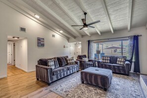 A spacious living room with a high ceiling, a ceiling fan, and a large window with curtains. - Near River! Home w/ Fenced Yard in Bullhead City (Bullhead City)