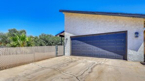 Eine Garage mit Betonauffahrt, einem Zaun aus Maschendraht und einem strahlend blauen Himmel.