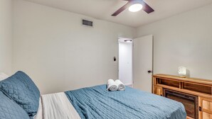 Ein Schlafzimmer mit Bett, Deckenventilator, einem Holzschrank und einer Tür zu einem anderen Raum.