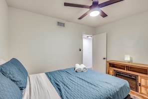 Un dormitorio con cama, ventilador de techo, cómoda de madera y puerta que da a otra habitación.