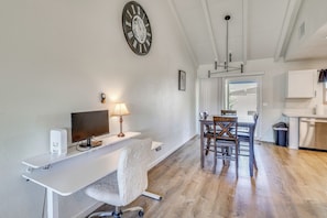 Eine moderne Küche mit weißen Schränken, einem Esstisch mit Stühlen, einer großen Uhr und einem Computerarbeitsplatz mit Lampe.