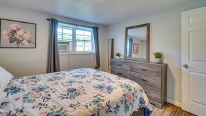 Een slaapkamer met een bloemenbed overtrek, een dressoir met lades, een spiegel en een raam met gordijnen.