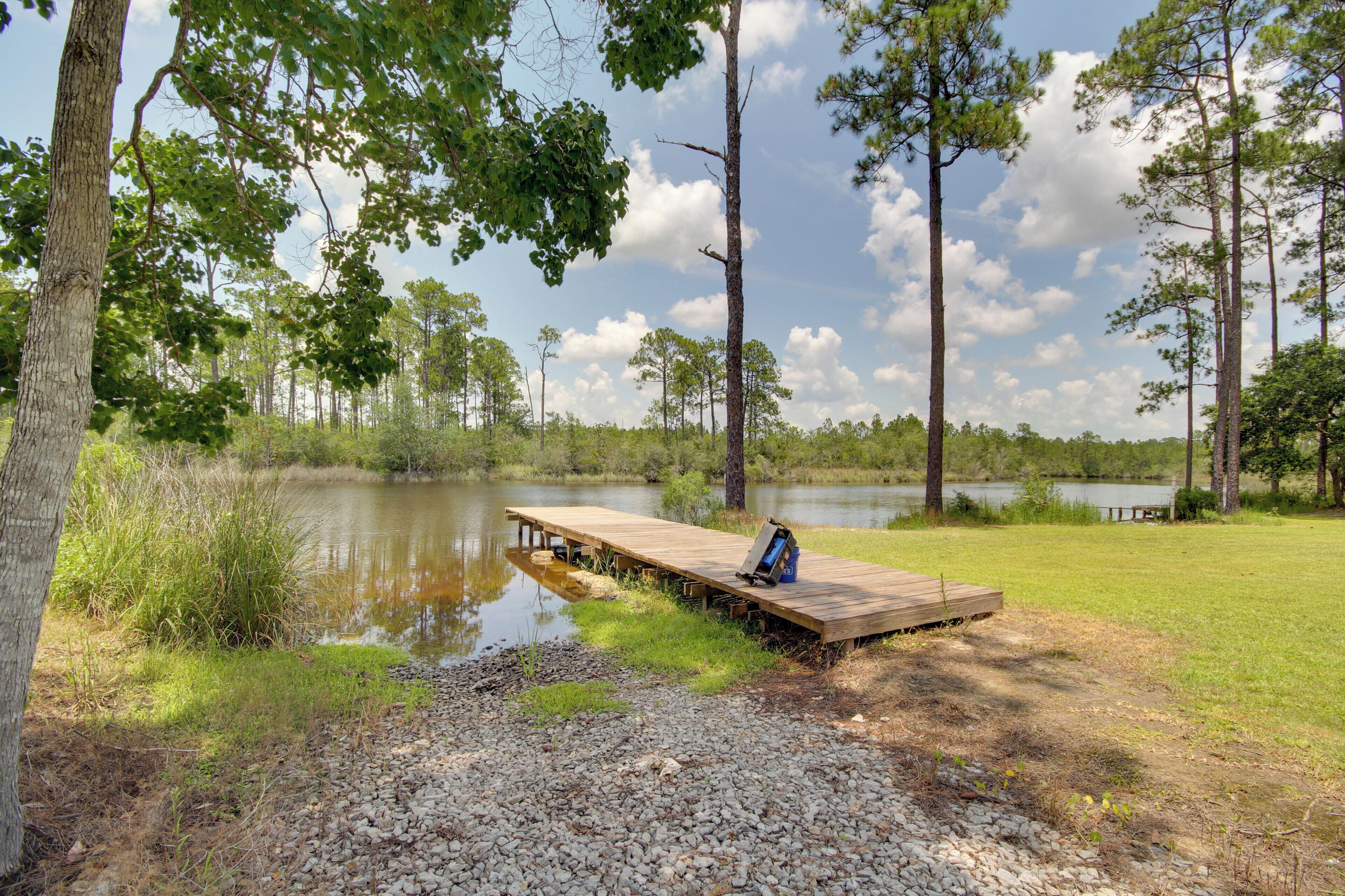 A wooden dock extending into a calm lake, surrounded by trees and grassy areas.