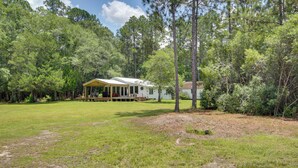 A single-story house with a covered porch, surrounded by a grassy yard and dense trees. - Private Ocean Springs Waterfront Retreat W/porch (Ocean Springs)