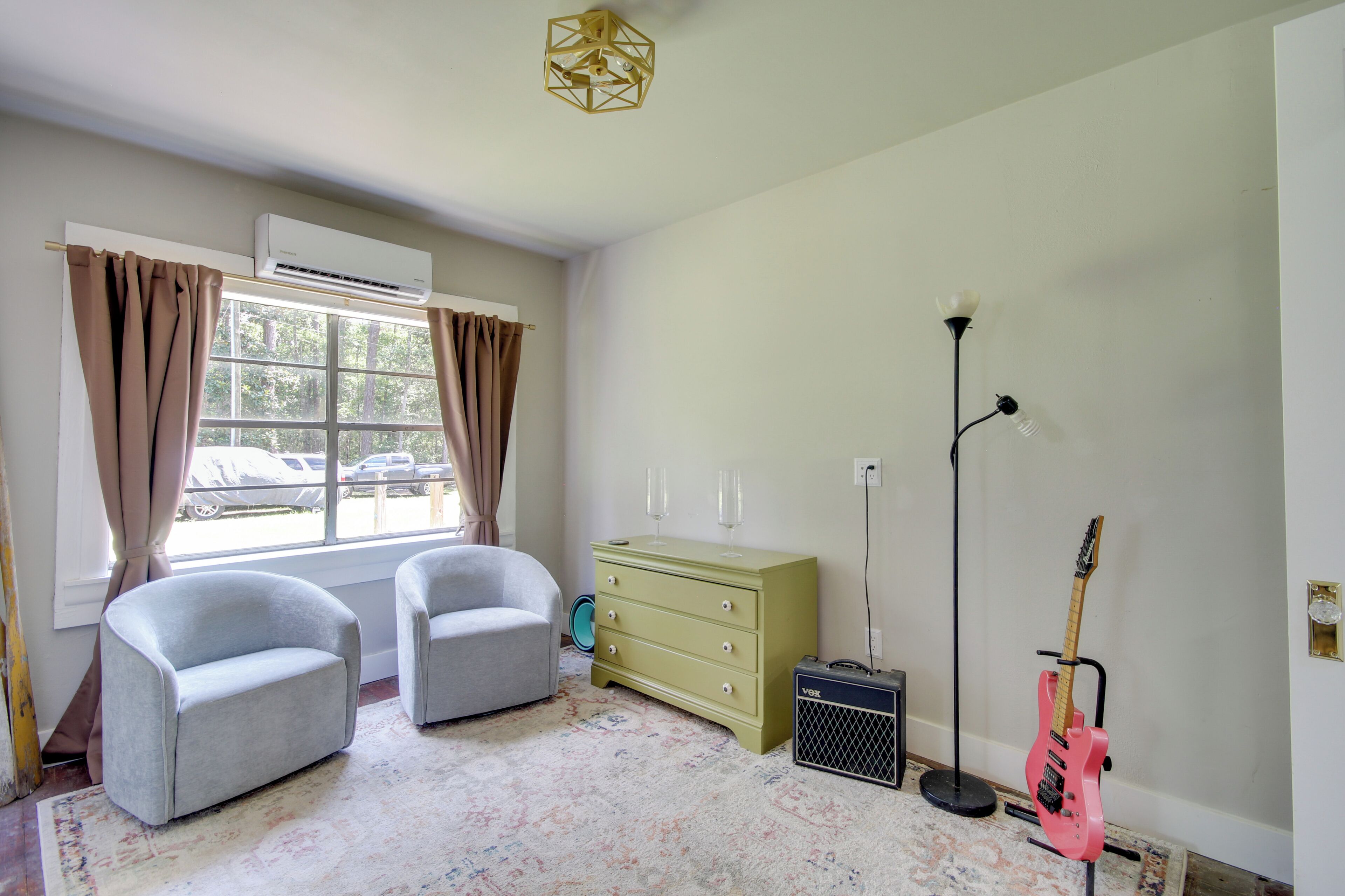 A room with two armchairs, a green dresser, a pink guitar, a floor lamp, and an air conditioning unit.