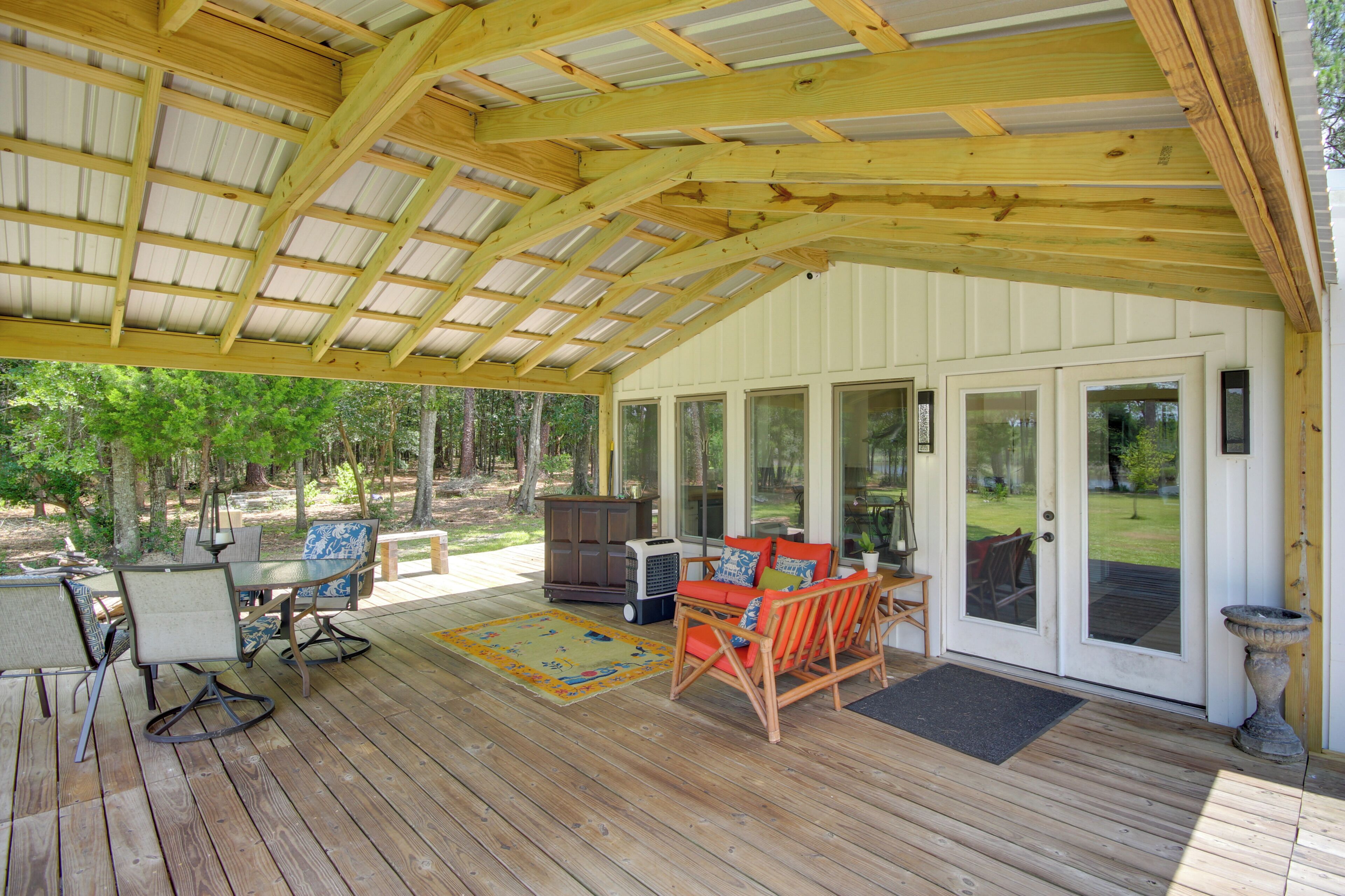 A covered outdoor area with wooden flooring, a table with chairs, a sofa, and a potted plant.