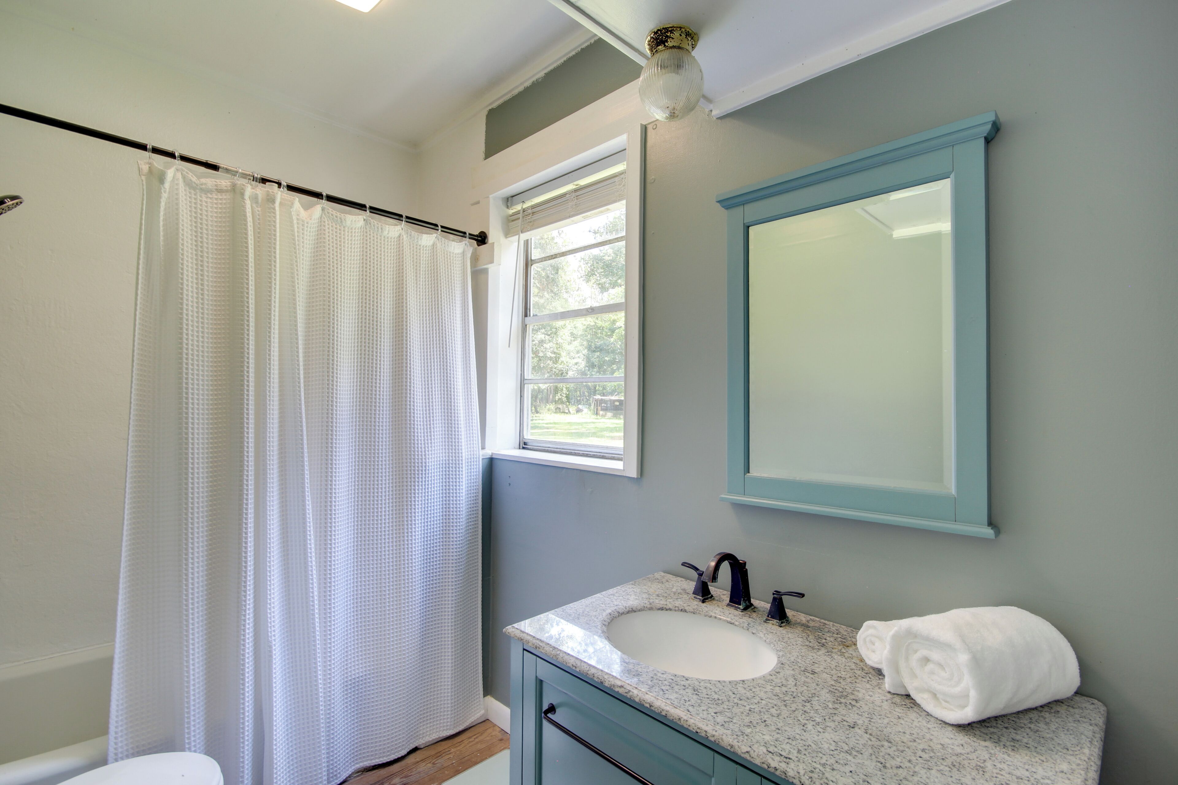 A bathroom with a shower curtain, a sink with a mirror, and a window.