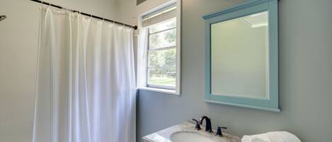 A bathroom with a shower curtain, a sink with a mirror, and a window.