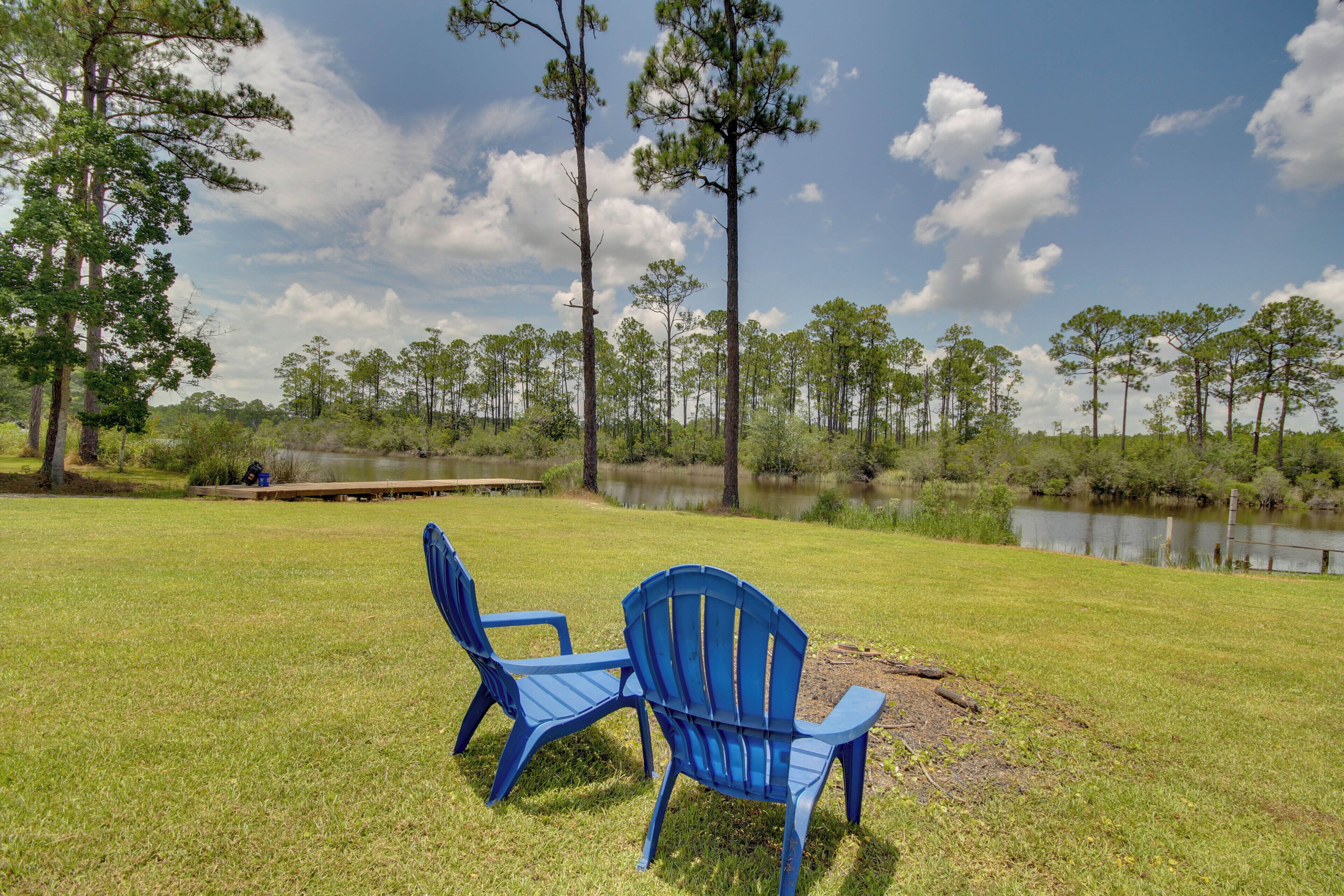 Twee blauwe Adirondack-stoelen op een gazon met een vijver en bomen op de achtergrond.