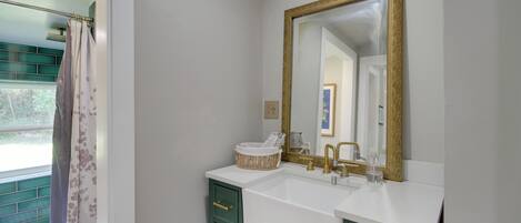 A bathroom with a white sink, a gold-framed mirror, and green cabinets.