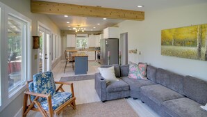 A modern living room with a grey sectional sofa, a wooden chair, and a large window. - Private Ocean Springs Waterfront Retreat W/porch (Ocean Springs)