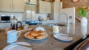 Une cuisine avec un mur en pierre, des meubles blancs, une cuisinière, une machine à café et une horloge.
