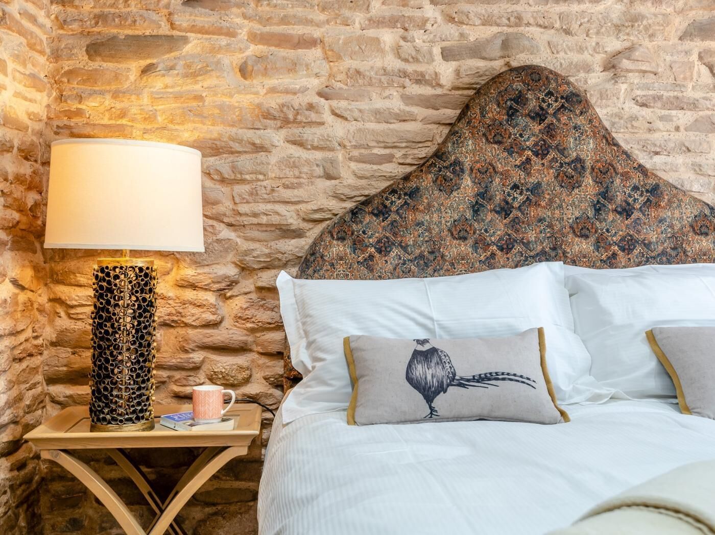 Een bed met een hoofdbord met patroon, een bedlamp en een mok op een nachtkastje van hout.