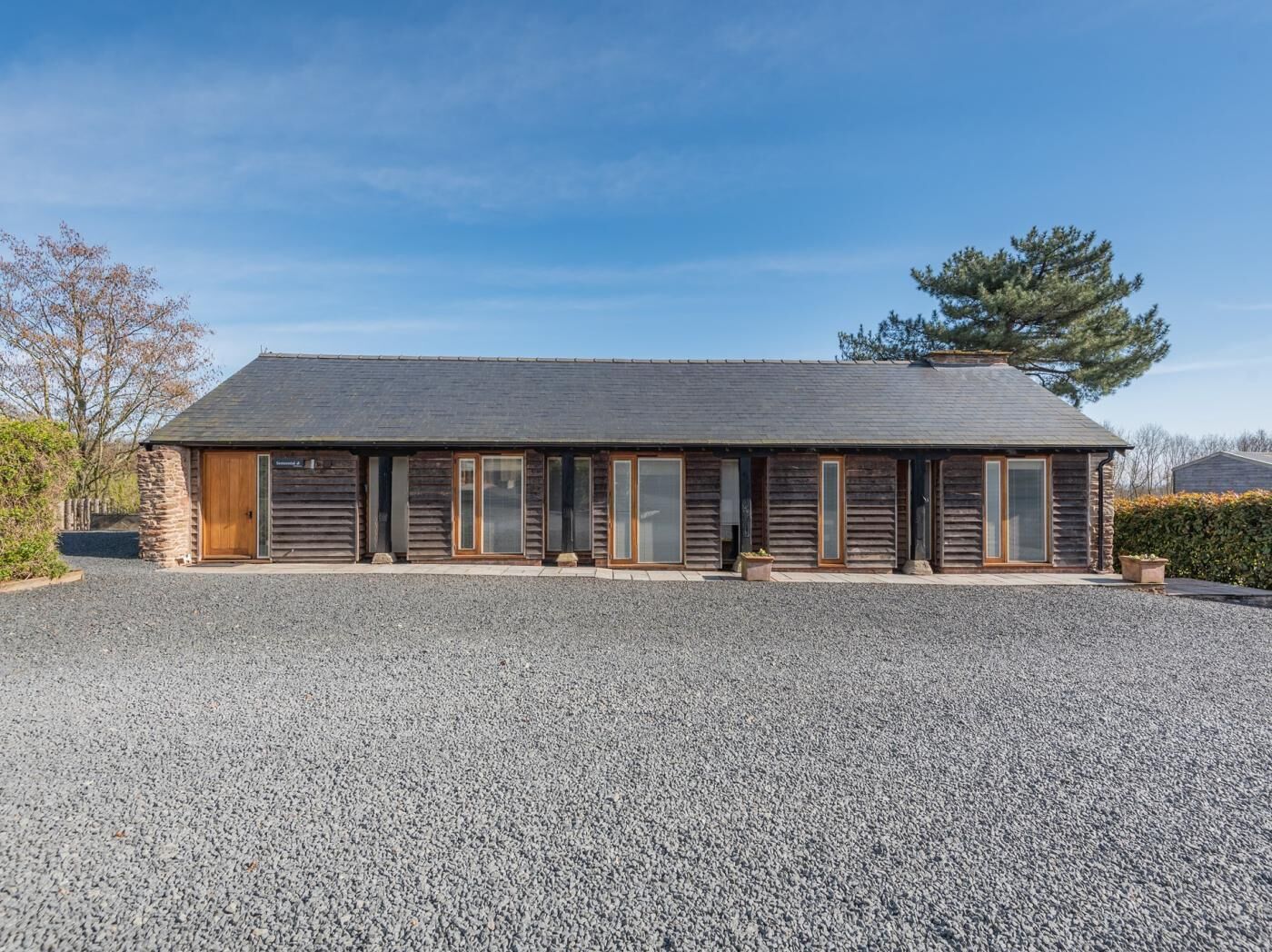 Une cabane en rondins avec une allée en gravier, des portes en bois et un mur de pierres sur un de ses côtés.