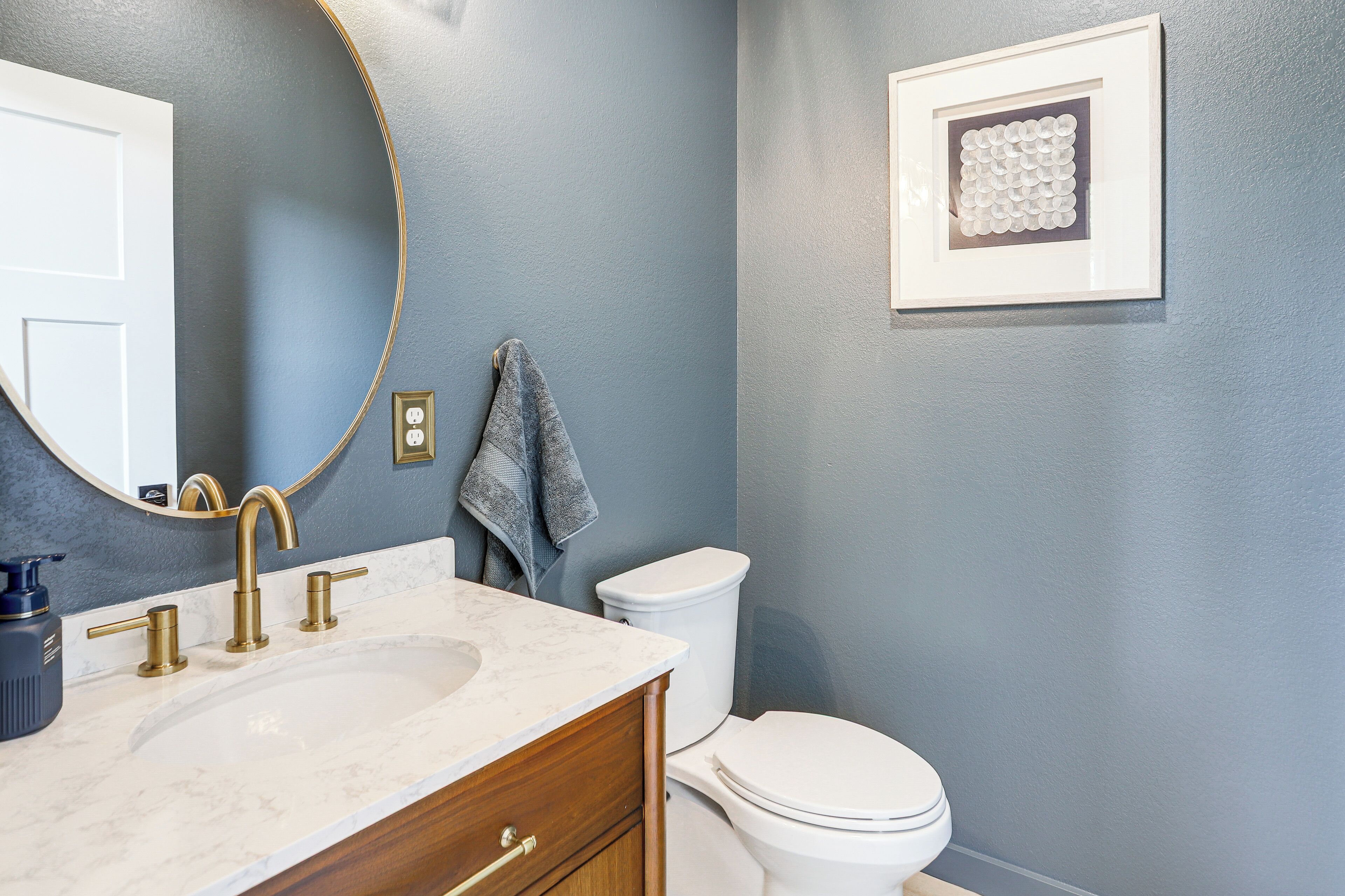 A bathroom with a white sink, gold faucet, and a white toilet.