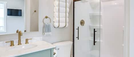 A bathroom with a marble sink, a toilet, a glass shower enclosure, and a towel rack with folded towels.
