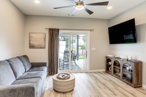 A living room with a sofa, a coffee table, a TV mounted on the wall, and a sliding glass door leading to an outdoor area. - Brand-new Relaxing River Retreat: Lake Erie Access (Port Clinton)
