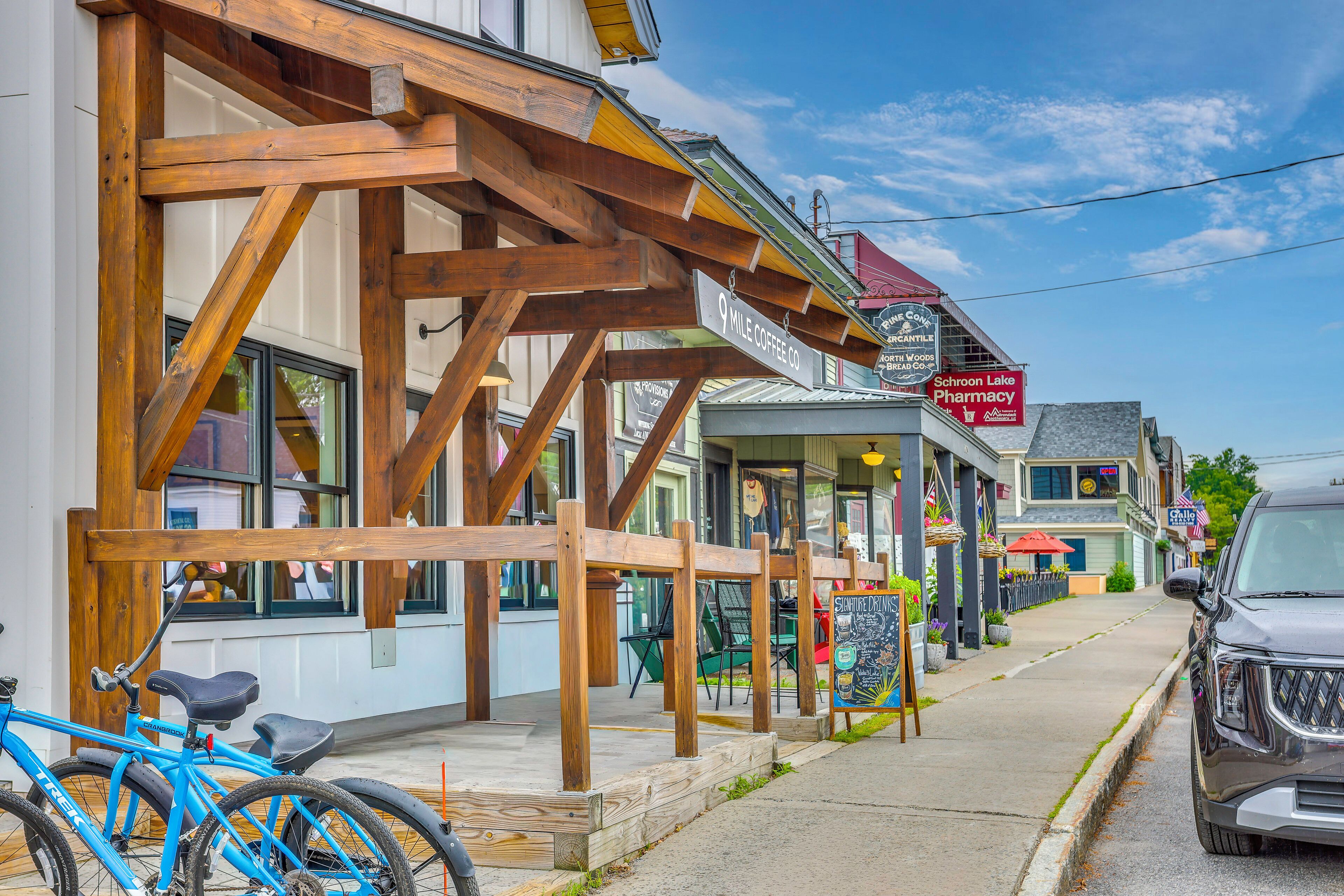 Vista de la calle con una bicicleta azul, una pérgola de madera y comercios, incluyendo una farmacia y una cafetería.