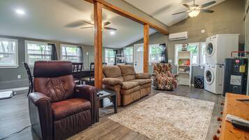 A spacious living room with a brown leather chair, a brown sofa, a wooden coffee table, a patterned rug, and a ceiling fan.