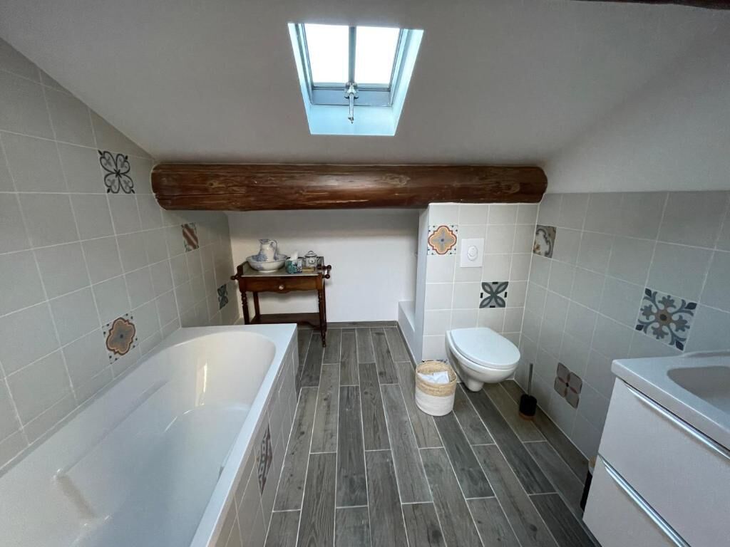 A bathroom with a skylight, a bathtub, a toilet, and a sink.