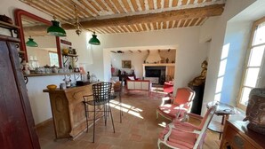 A rustic interior with a tiled floor, a wooden bar area, and a seating area with chairs.
