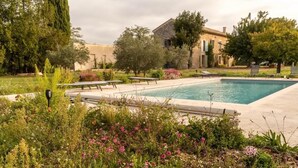 A swimming pool with lounge chairs, surrounded by greenery and a building in the background.