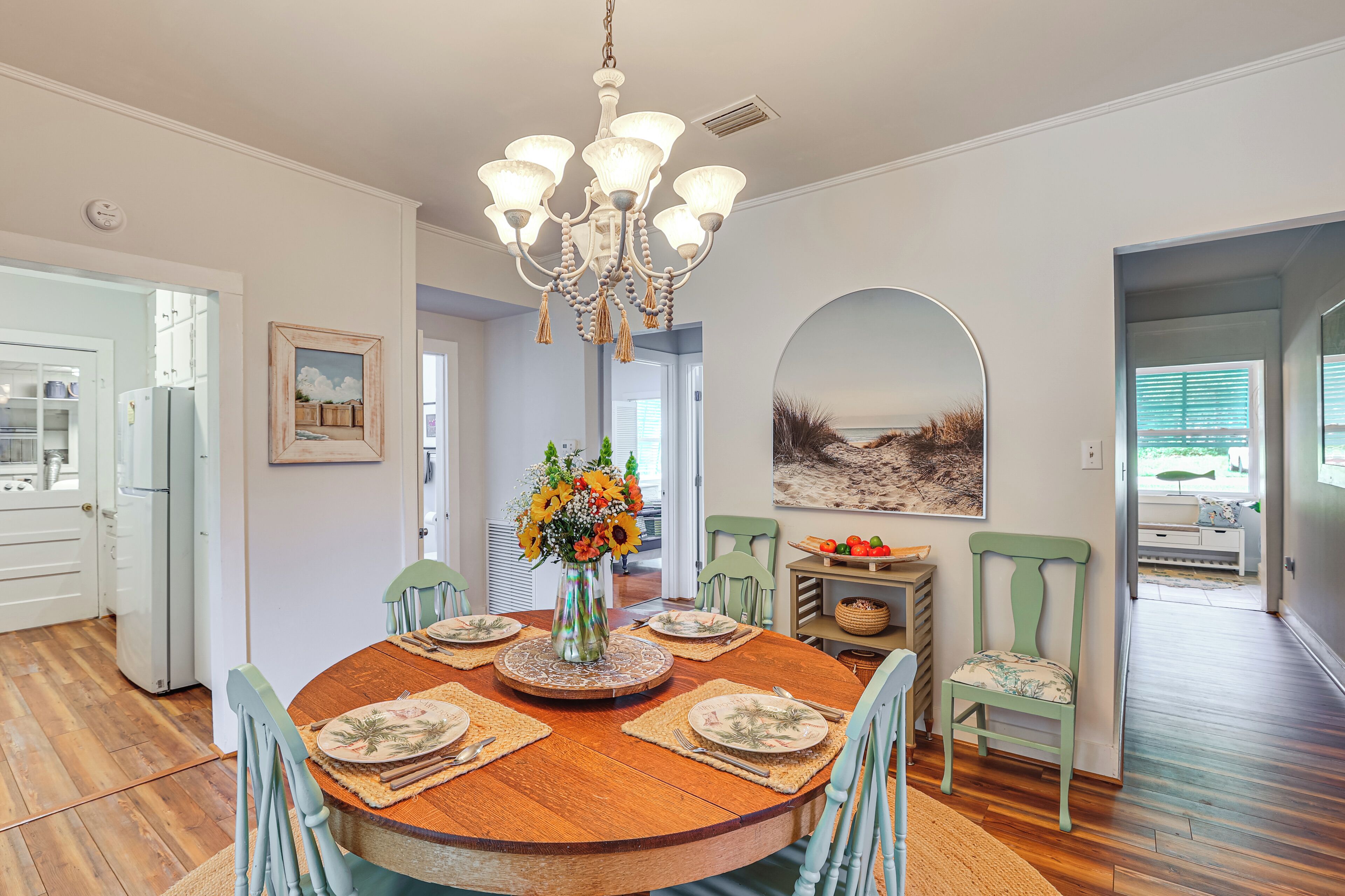 A dining room with a wooden table, chairs, a chandelier, and a vase with flowers.