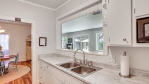 A kitchen with a double sink, a window with a view, and a dining area with a table and chairs. - Palm Cottage: Walk to Darien Waterfront & Fort (Darien)