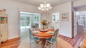 A dining room with a wooden table, chairs, a chandelier, and a view through a glass door. - Palm Cottage: Walk to Darien Waterfront & Fort (Darien)