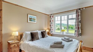 Un dormitorio con cama, mesitas de noche, una ventana con cortinas, un cuadro en la pared y vistas al exterior.
