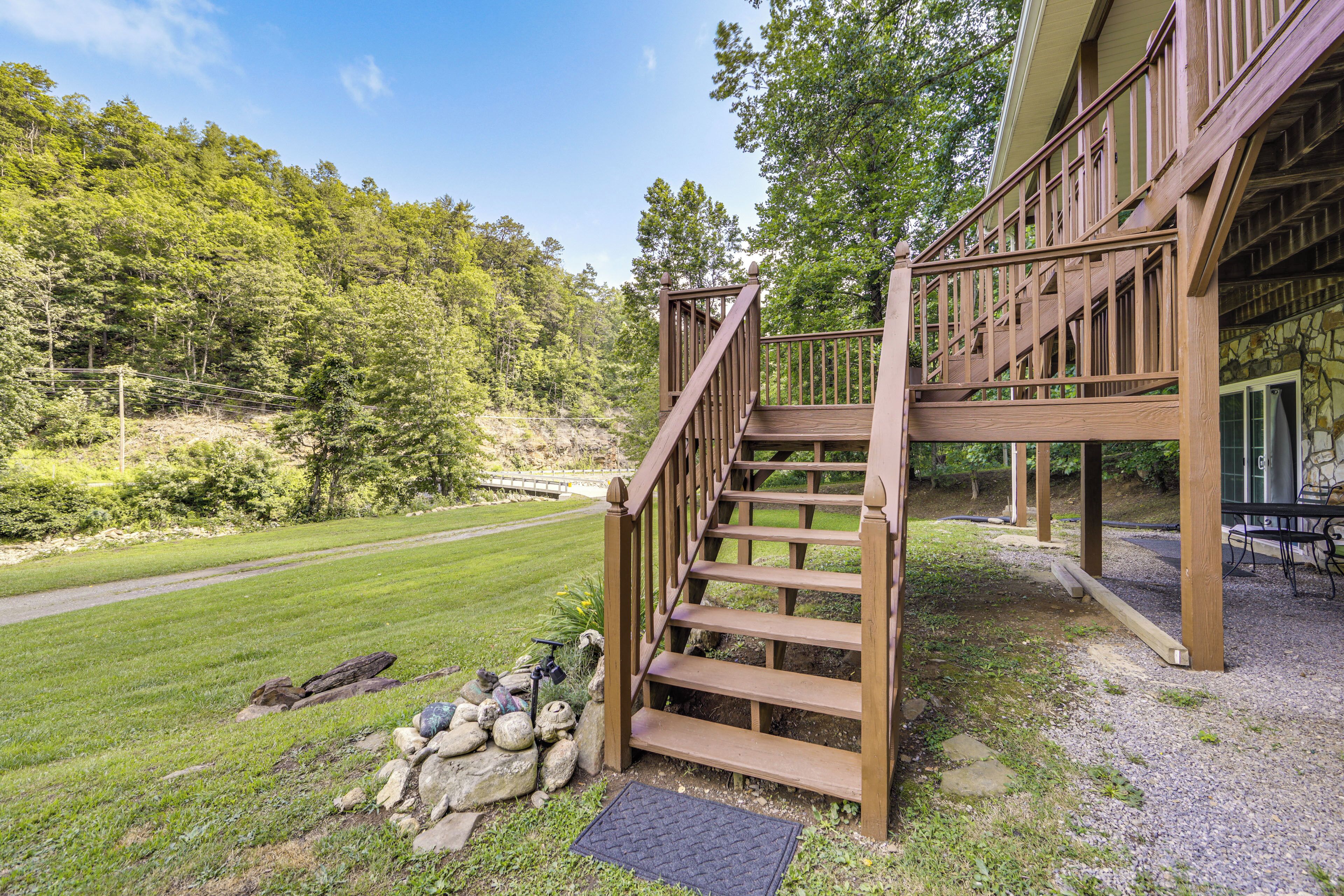 A wooden staircase leading to a building with a stone facade, surrounded by a grassy area and trees.