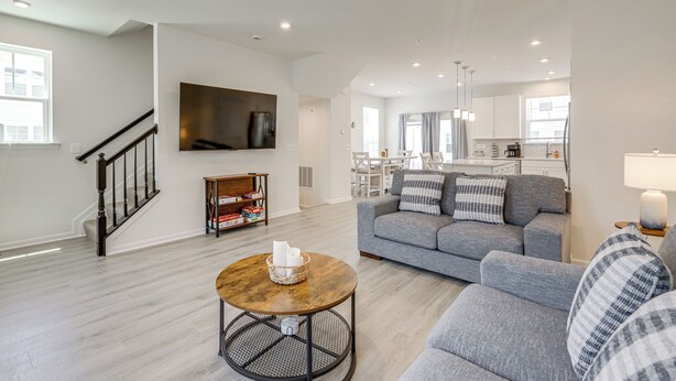 A modern living room with a grey sofa, a coffee table, and a TV mounted on the wall. - Walk to Cambridge Waterfront: Townhome w/ Deck (Cambridge)