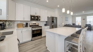 A modern kitchen with white cabinetry, stainless steel appliances, and a central island with bar stools. - Walk to Cambridge Waterfront: Townhome w/ Deck (Cambridge)