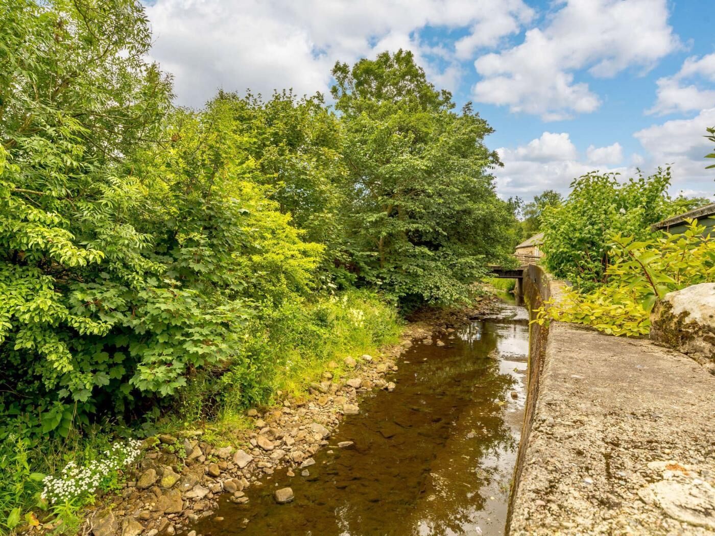 Un étroit canal bordé d’une végétation luxuriante et surmonté d’un pont de pierre.