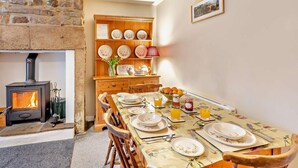 A cozy dining area with a stone fireplace, wooden shelves with plates, and a table set for two with fruit and drinks. - 2 Bed in Hexham (oc-50500) (Bellingham)